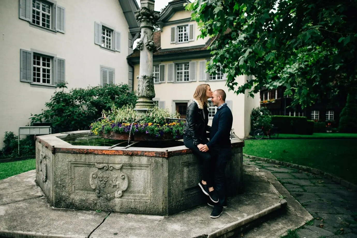 Liebesgeschichte. Ein junges verliebtes Paar küsst in der Nähe eines schönen Brunnens mit Blumen.